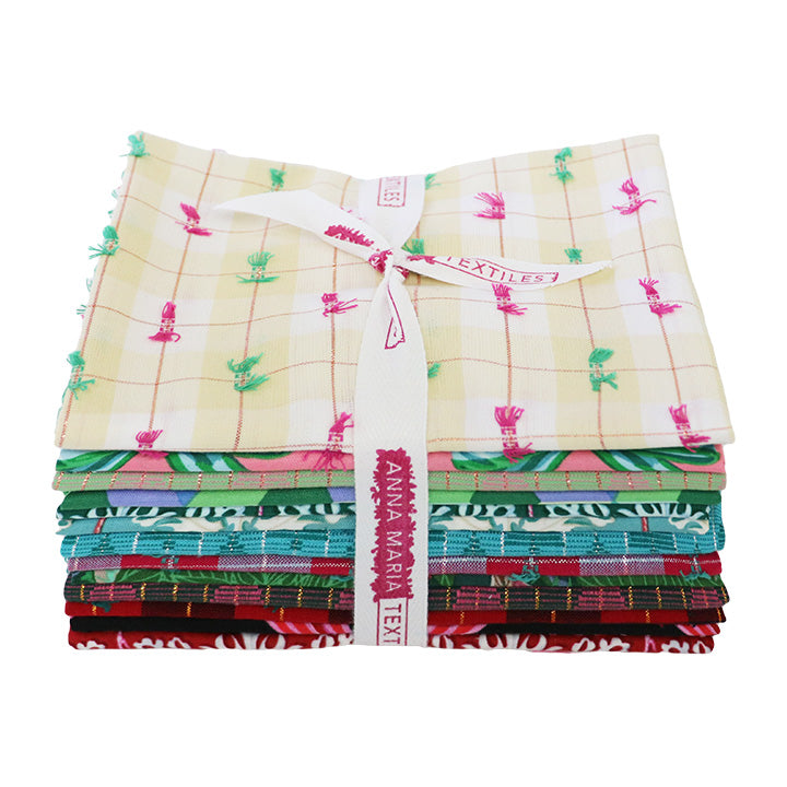Stacked bundle of colorful patterned fabrics tied with white “Anna Maria Textiles” ribbon, featuring floral and geometric designs.