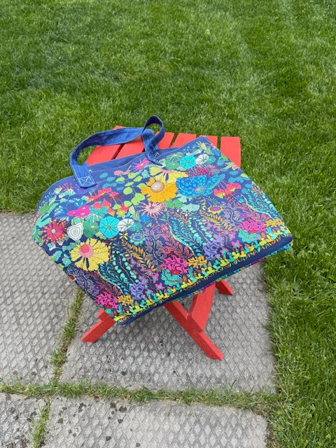 Completed Sunshine Carry All tote bag made from Sally Kelly for Windham Fabrics canvas panel, displayed on a red folding chair outdoors
